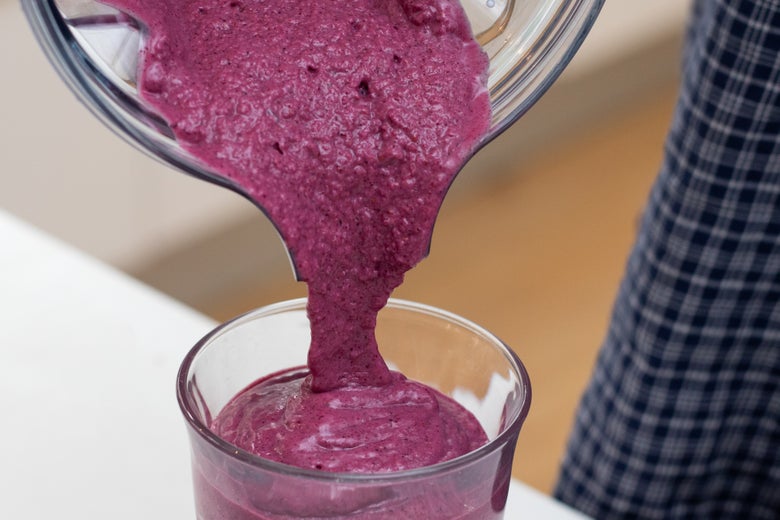 Smoothie mixture being poured from the blender into a cup.